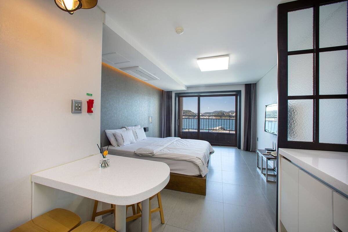 Een hotelkamer met een bed, een bureau, een stoel, een klein tafeltje, een raam met uitzicht op zee en een balkon.