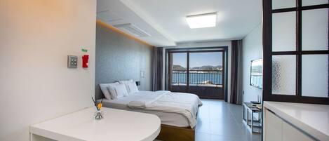 Habitación de hotel con cama, escritorio, silla, mesita y ventana con vista al mar, además de un balcón.
