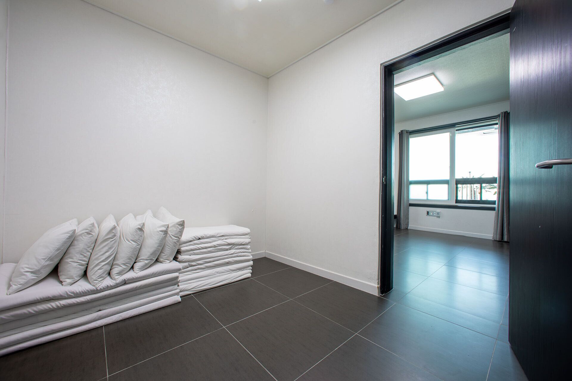 A hotel room with a neatly stacked pile of white pillows and a dark tiled floor.