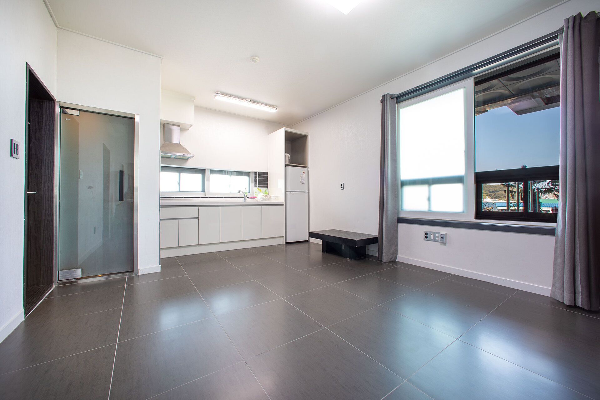 A modern kitchen with white cabinets, a built-in oven, and a window with a view of a park.