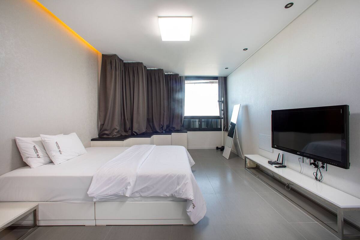 Een moderne hotelkamer met een bed, een flatscreen televisie, een raam met gordijnen en een plafondlamp.