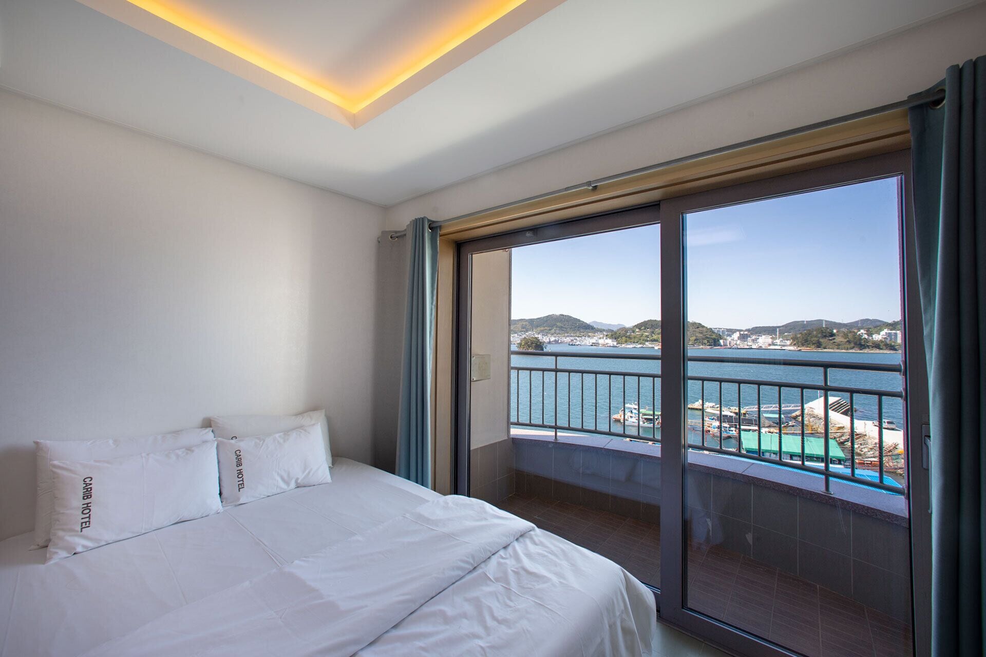 Una camera d'albergo con un letto, un'ampia finestra e vista su un lago e degli edifici.