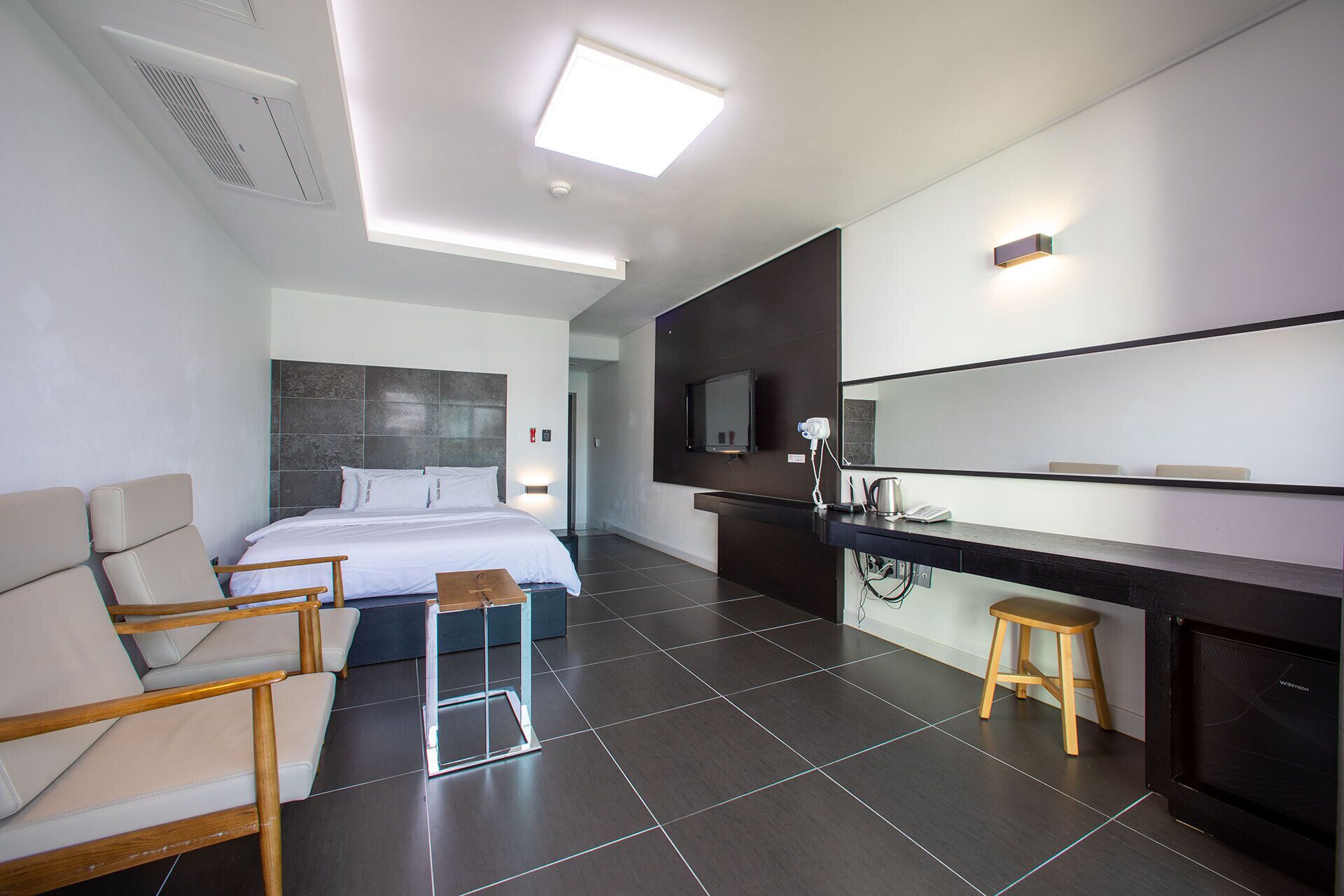 Habitación de hotel moderna con cama, sofá, escritorio con espejo y baño visible a través de una puerta abierta.