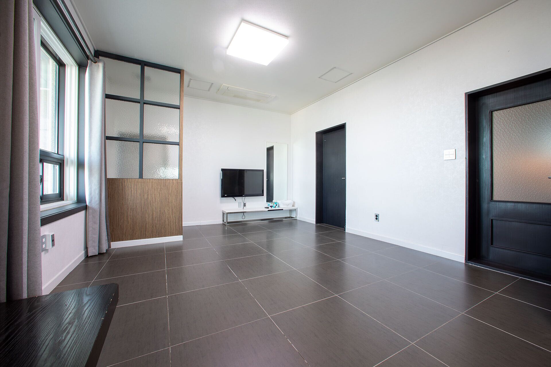 A spacious, modern hallway with dark tiled flooring, a flat-screen TV mounted on the wall, and a dark door on the right.