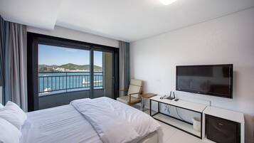 A hotel room with a bed, a TV, a desk, and a view of the sea.