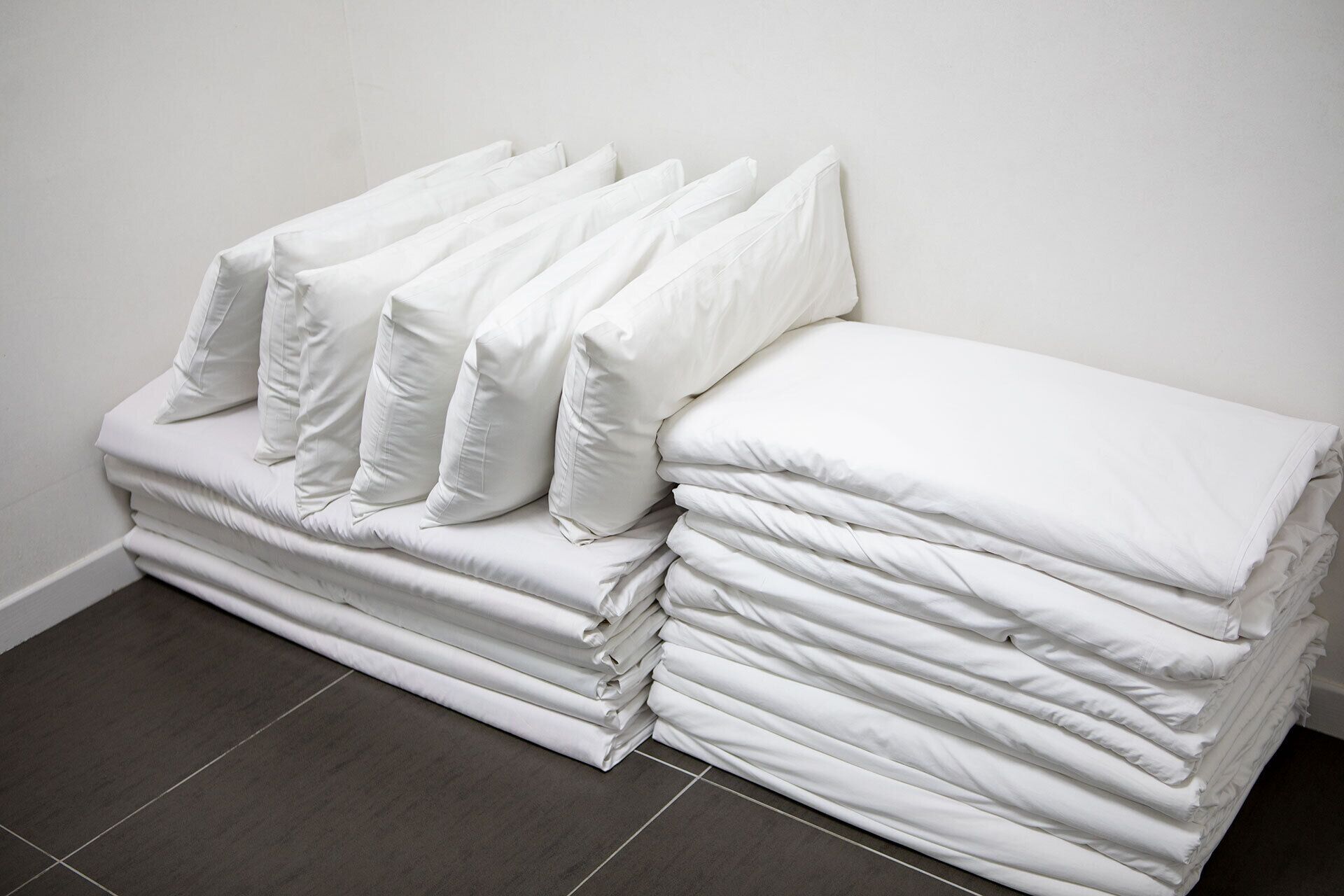 Un montón de colchones y almohadas blancos apoyados contra una pared.