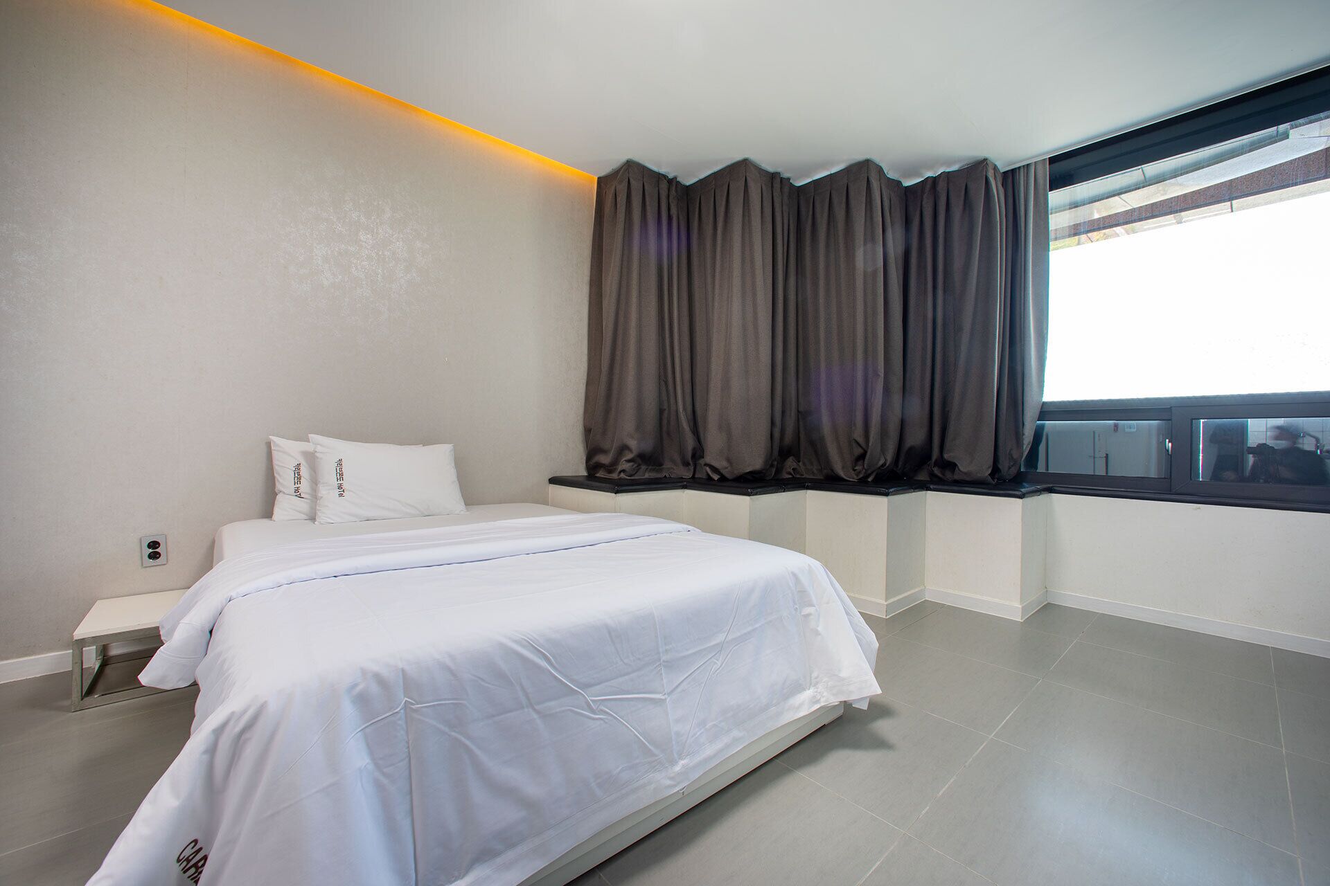 Una habitación de hotel moderna con una cama grande, una ventana con cortinas oscuras y vistas a la ciudad.