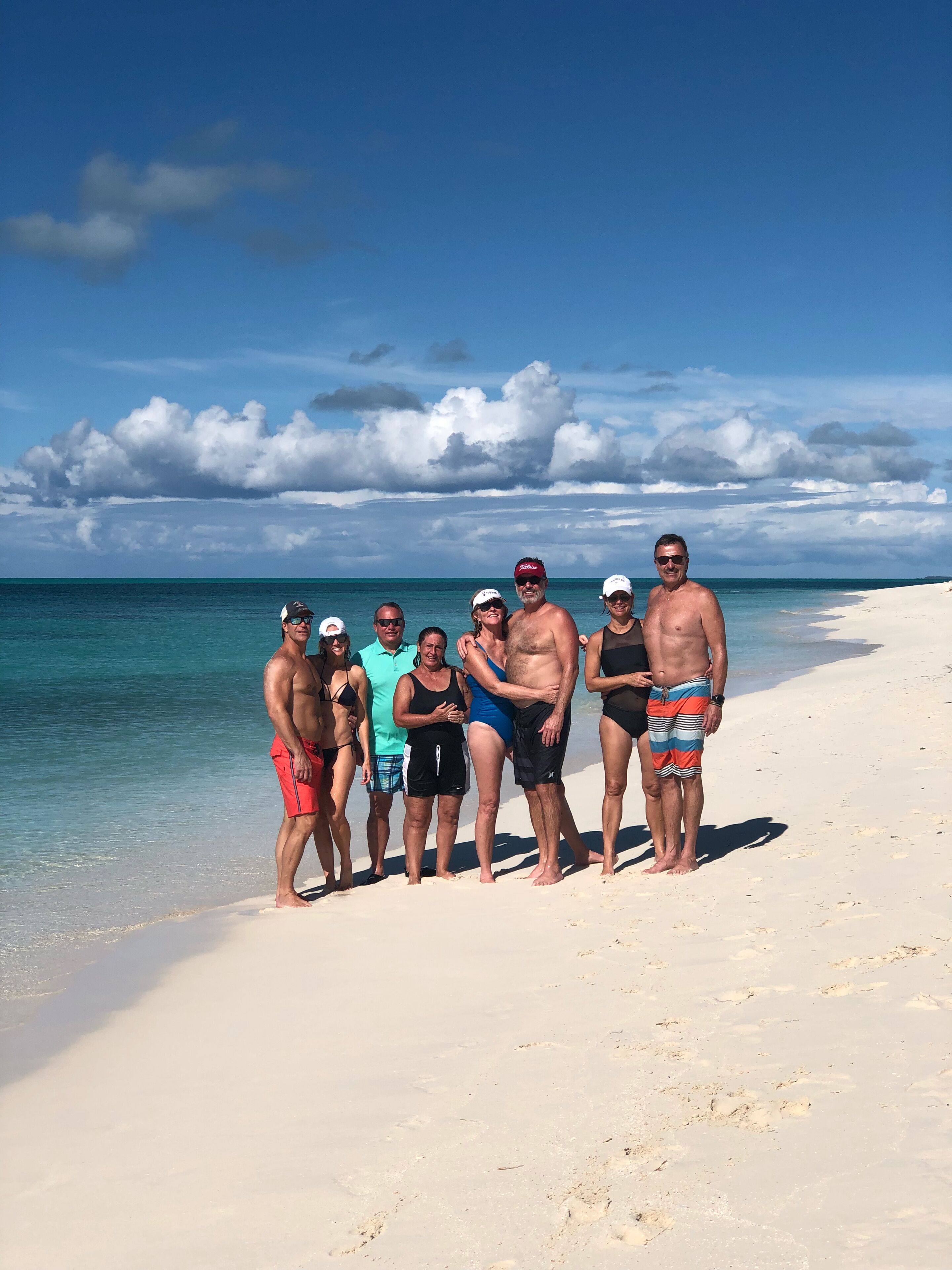 A group of people standing on a sandy beach with a clear blue sky and ocean in the background.