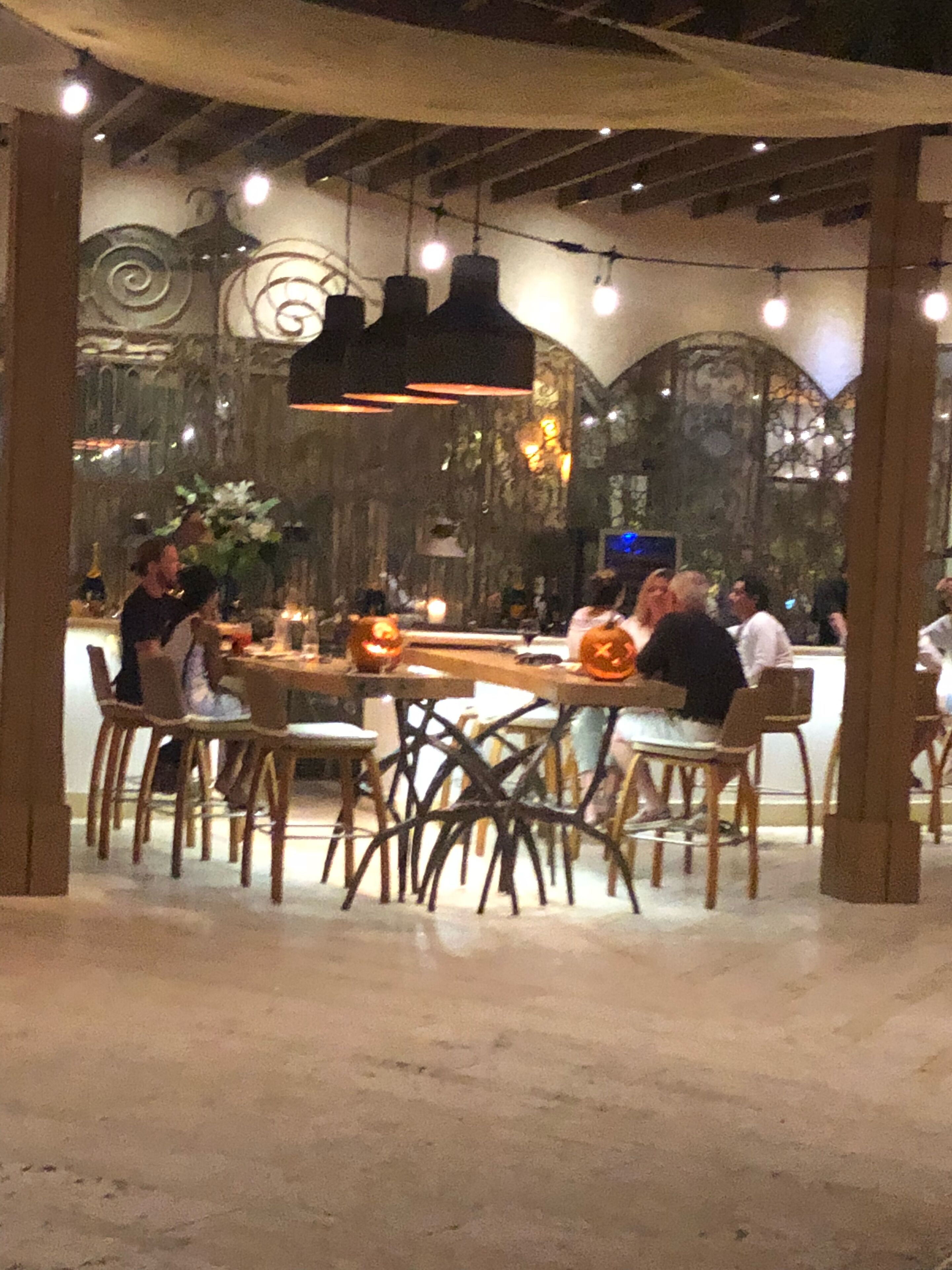 Un comedor interior con mesas y sillas de madera, un techo alto con vigas a la vista e iluminación decorativa.