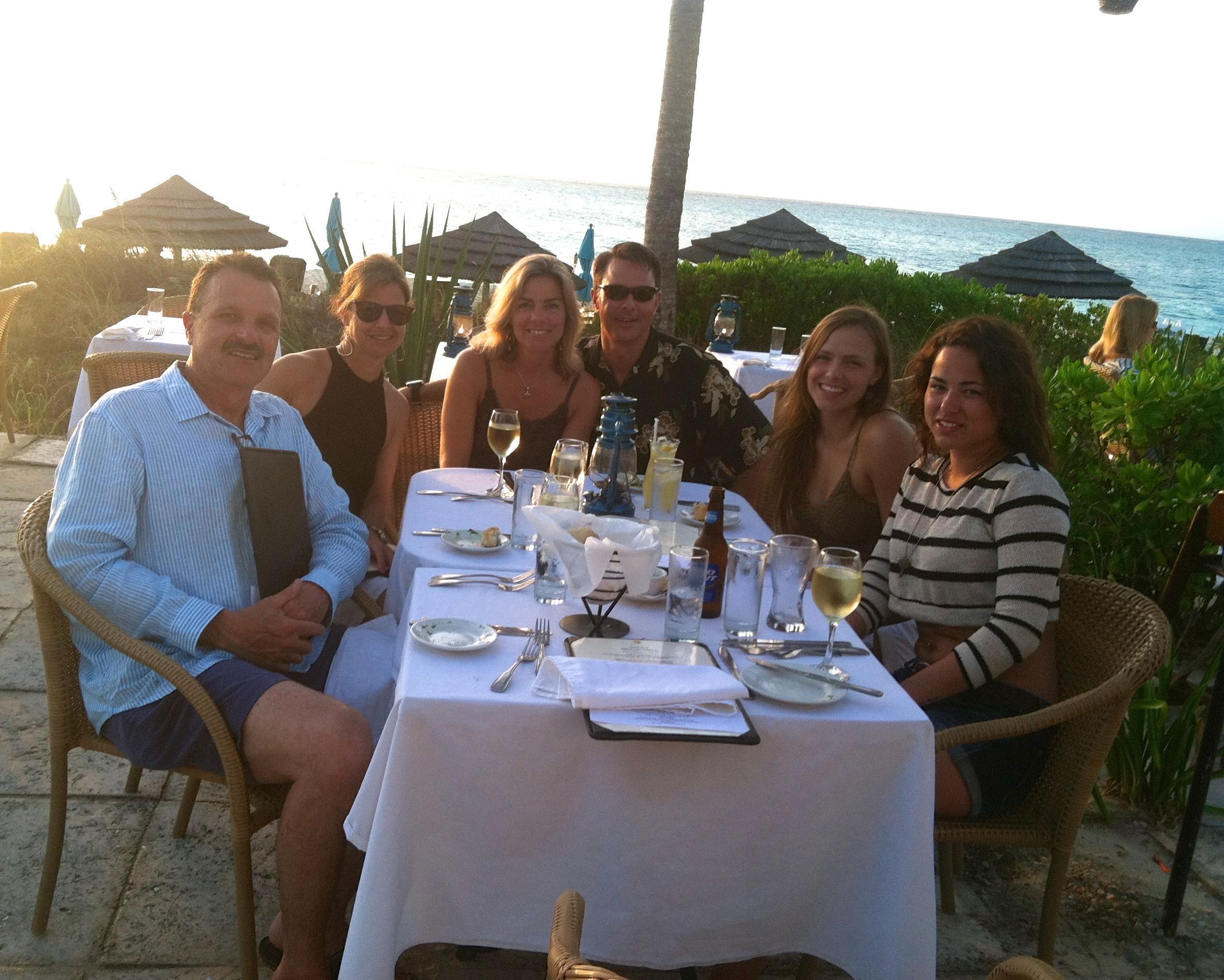 Un groupe de personnes est assis à une table en plein air, devant laquelle s’étend une vue sur l’océan.