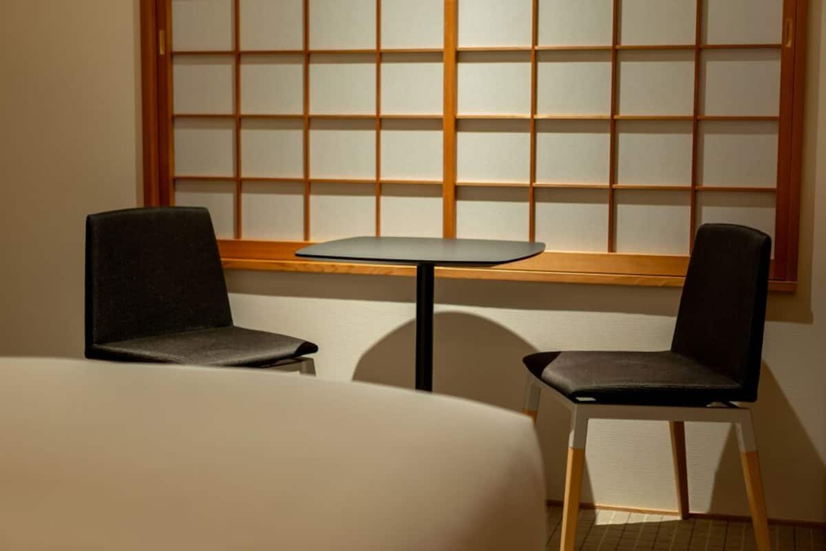 A room with a low table and two chairs, a window with a grid pattern, and a wooden frame.
