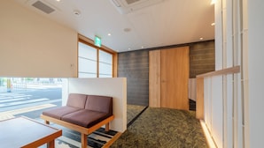 A modern hotel room with a sofa, a small table, a patterned carpet, and a view of the street. - RESI STAY Hachi Inn (Kyoto)