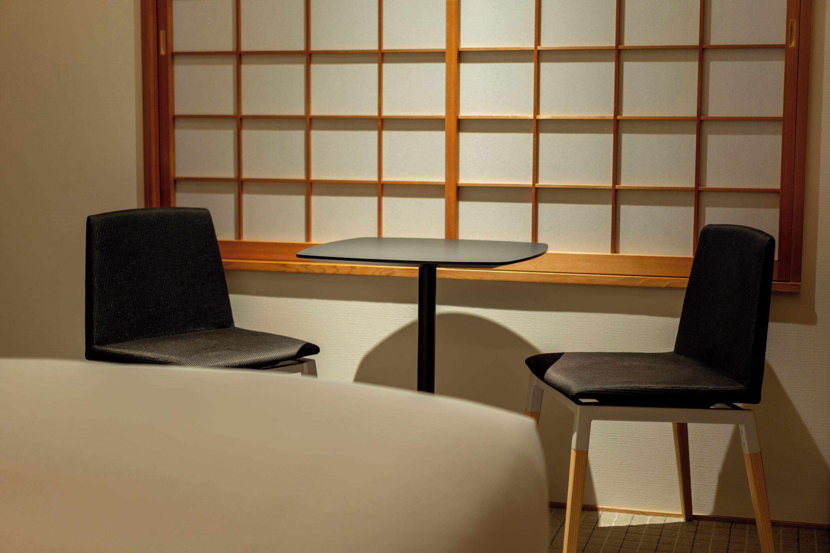 A room with a low table and two chairs, a wooden window with a grid pattern, and a plain wall.