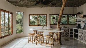A modern kitchen with large windows, wooden stools, and a central island.