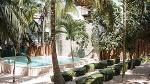 A pool area with a sandy floor, surrounded by palm trees and green seating.