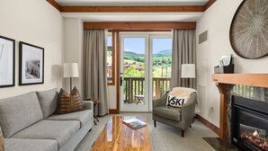 A living room with a sofa, armchair, coffee table, fireplace, and a balcony with a scenic view.