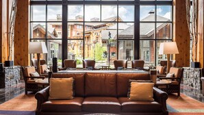 A lobby with a leather sofa, multiple chairs, a coffee table, and a large window offering a view of buildings and a stone wall.