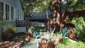 A garden with a wooden deck, green chairs, and a variety of plants.