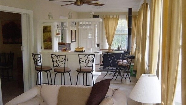 A living room with a sofa, a table with a lamp, and a kitchen area in the background.