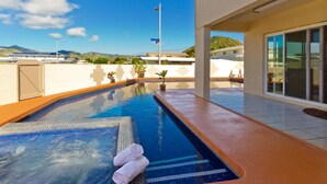 A swimming pool with a tiled edge, a towel on the edge, and a view of a building and mountains in the background.