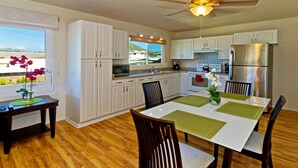A modern kitchen with white cabinets, a stainless steel refrigerator, and a dining area with a white table and chairs.