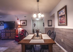 Cozy dining area with a table for four, featuring a chandelier, TV, and comfortable seating.