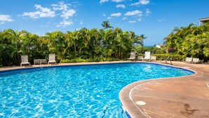 Une piscine d’un bleu éclatant, entourée de chaises longues et de palmiers, avec l’océan en toile de fond.