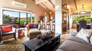 Un vaste espace de vie avec une grande porte-fenêtre donnant sur un balcon, un ventilateur de plafond et une cuisine moderne en arrière-plan.