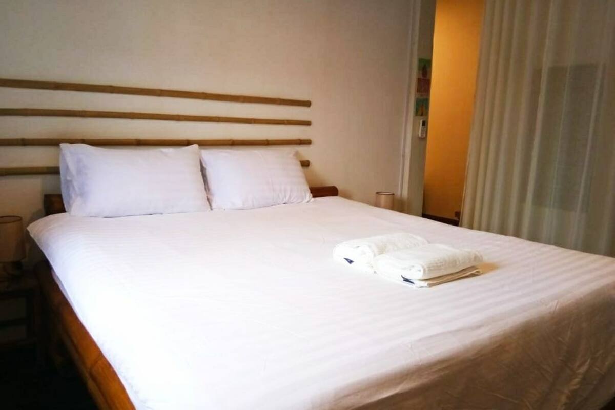 A hotel room with a large bed, two pillows, a neatly folded white towel, and a wooden headboard.