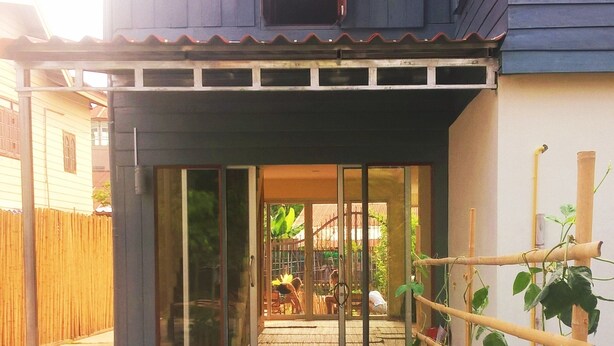 Une maison moderne dotée d’une grande porte vitrée, d’une terrasse en bois et d’un jardin où poussent des œillets d’Inde et des plants de tomates.