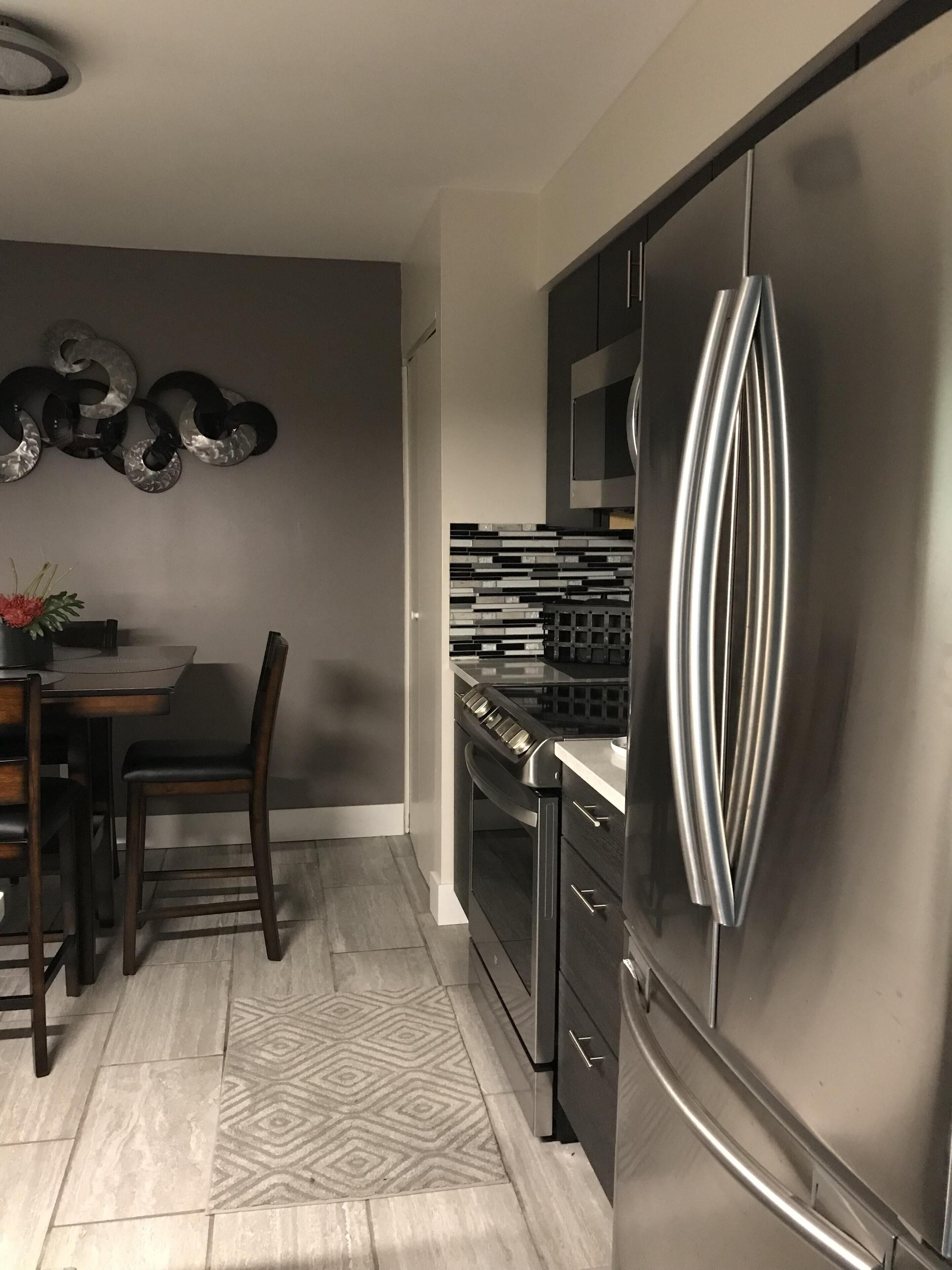 A modern kitchen with a stainless steel refrigerator, a dining table with chairs, and a decorative wall piece.