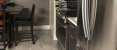 A modern kitchen with a stainless steel refrigerator, a dining table with chairs, and a decorative wall piece.