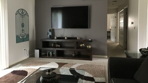 A modern living room with a flat-screen TV mounted on the wall, a dark entertainment unit below, and a patterned rug on the floor. - Newly renovated with lots of upgrades. (Portage)