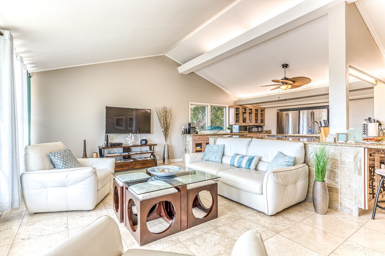 A spacious living room with a large flat-screen TV, a glass coffee table, and a white sofa.