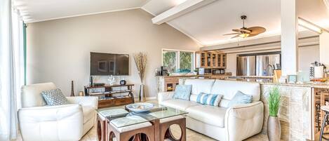 A spacious living room with a large flat-screen TV, a glass coffee table, and a white sofa.