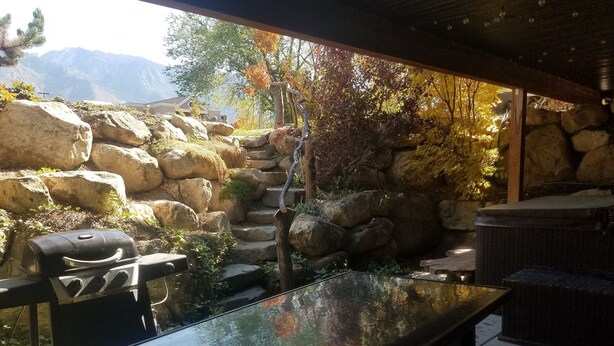 A stone patio with a grill, a small pond, and a view of mountains. - Great Sandy apartment with hot tub and pool table! (Sandy)