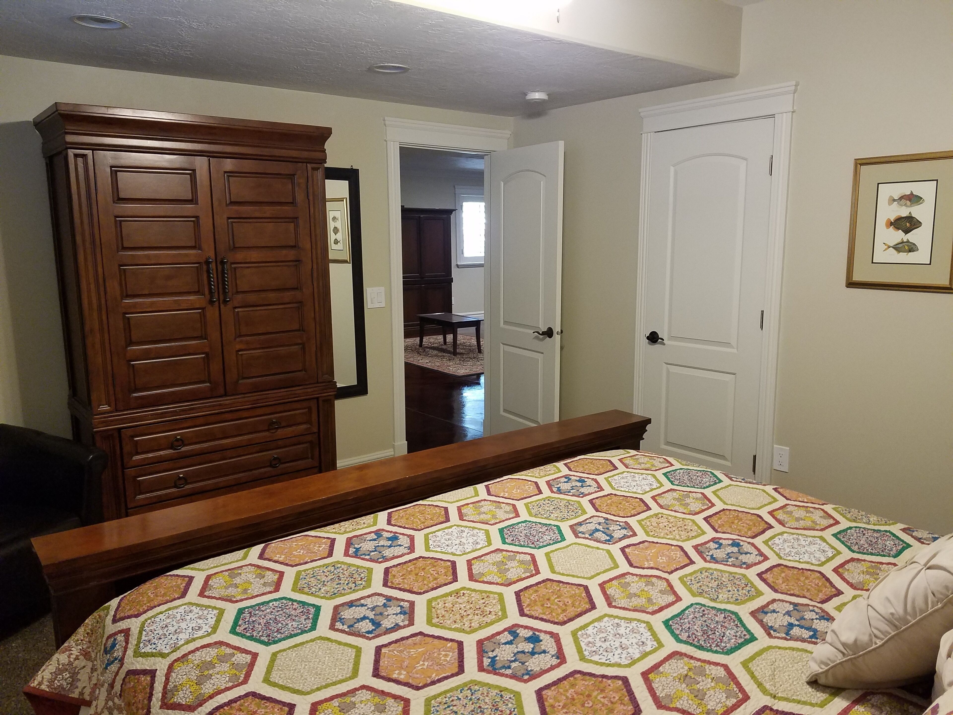 A bedroom with a large wooden wardrobe, a bed with a colorful hexagonal patterned bedspread, and a framed fish picture on the wall.