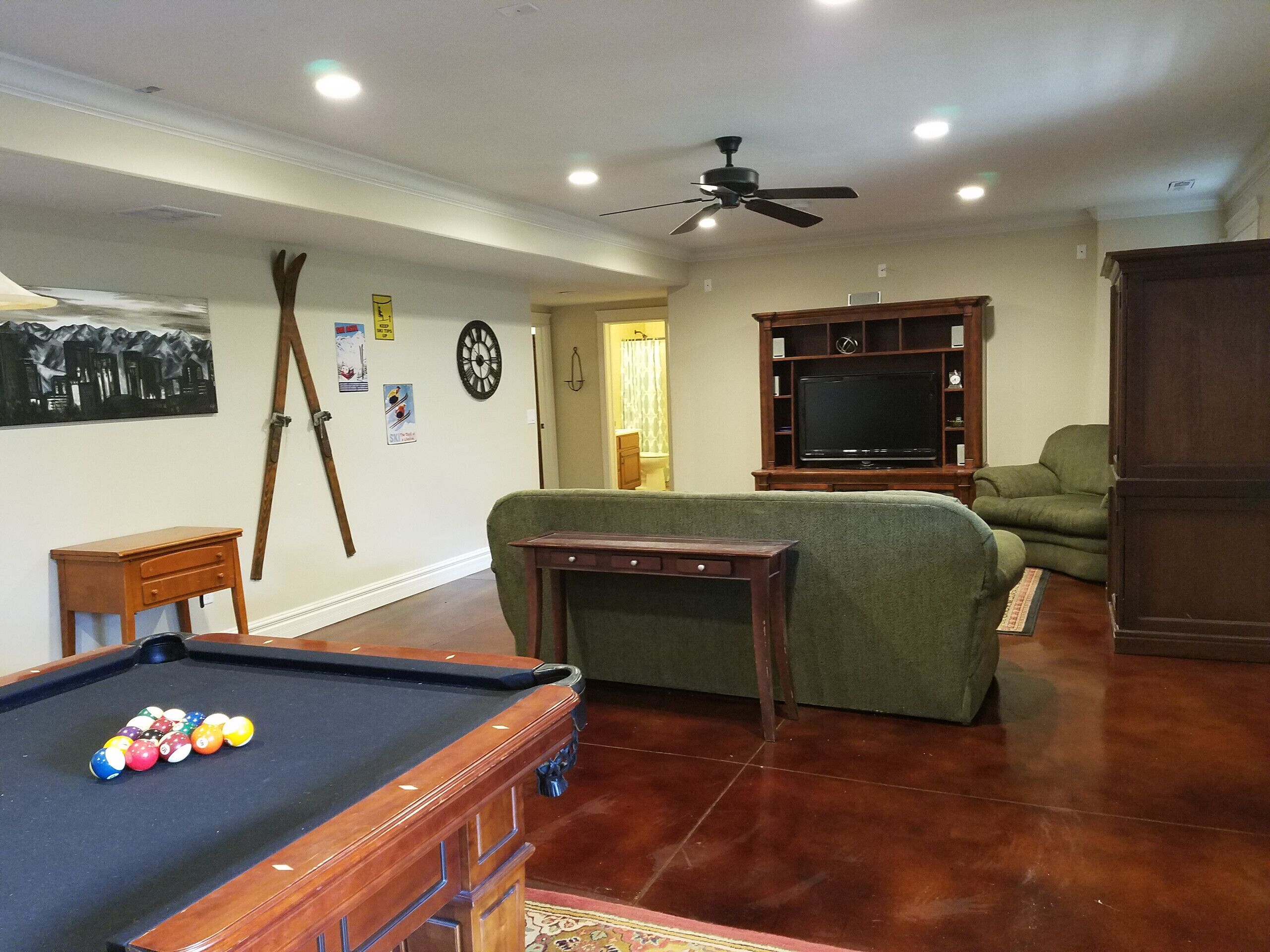 A living room with a pool table, green sofa, and a TV on a wooden stand.