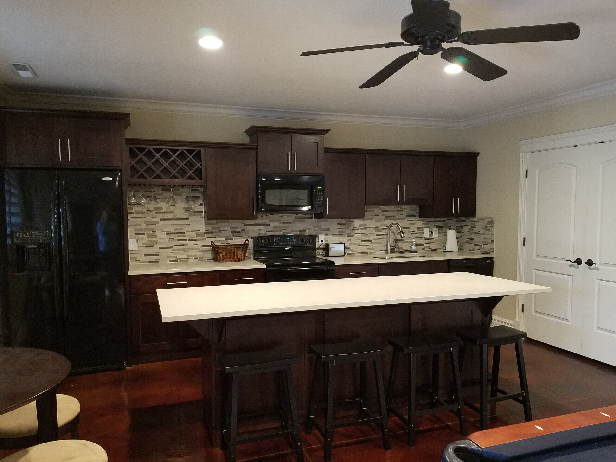 Una cocina moderna con armarios de madera oscura, encimera blanca, refrigerador negro, microondas y ventilador de techo.