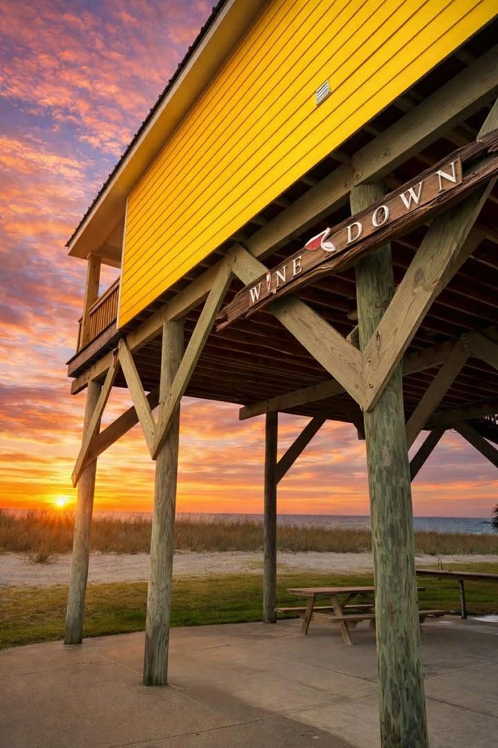 Una estructura de madera con un letrero que dice 'WINE CROWN' y un atardecer al fondo.