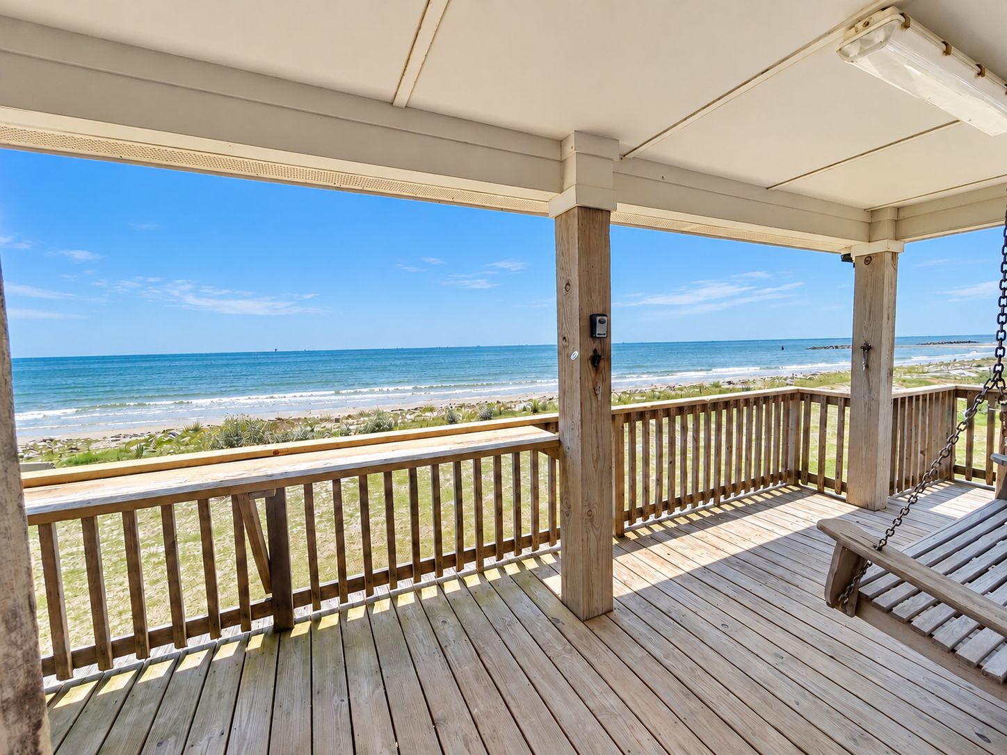 Eine Holzterrasse mit einer Schaukel, die Blick auf einen Strand mit dem Ozean und einem Sandufer bietet.
