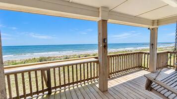 Eine Holzterrasse mit einer Schaukel, die Blick auf einen Strand mit dem Ozean und einem Sandufer bietet.