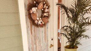 Een deur met een decoratieve krans, een bloempot op een metalen standaard en een deurmat met een patroon.