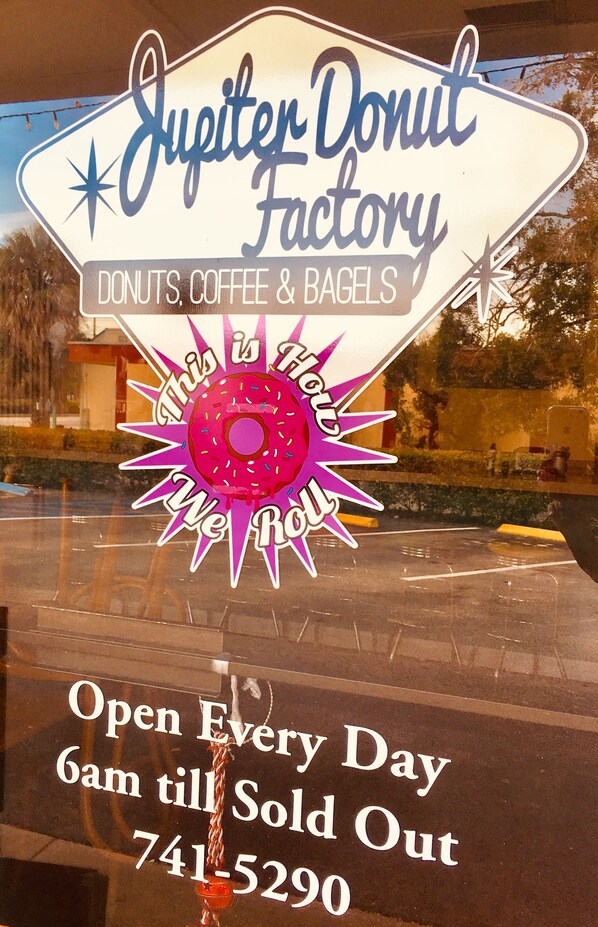 A neon sign for Jupiter Donut Factory advertising donuts, coffee, and bagels, with a note that it's open every day from 6am till sold out and a contact number.