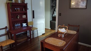 A dining area with a wooden table, chairs, a bookshelf, and a door leading to a kitchen.