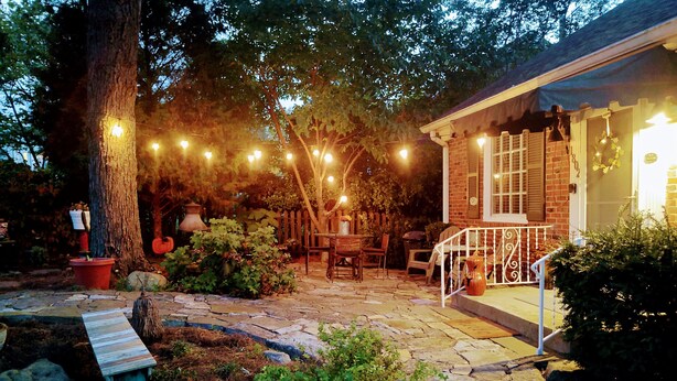 A stone patio with a rustic outdoor seating area, a wooden bench, and string lights.
