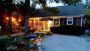 A house with a gravel driveway, a porch with outdoor seating, and a well-lit garden area.