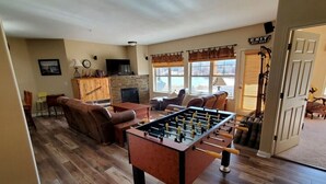 Ein gemütliches Wohnzimmer mit Tischfußball, bequemen Sitzgelegenheiten, einem Kamin und Blick ins Freie.