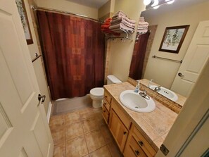 A bathroom with a shower curtain, a toilet, a sink with a mirror, and towels on a rack. - Beautiful Spacious Condo. (Fraser)