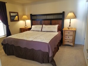 A neatly made bed with a patterned bedspread, two bedside lamps, a wooden nightstand, and a mirror on the wall. - Beautiful Spacious Condo. (Fraser)